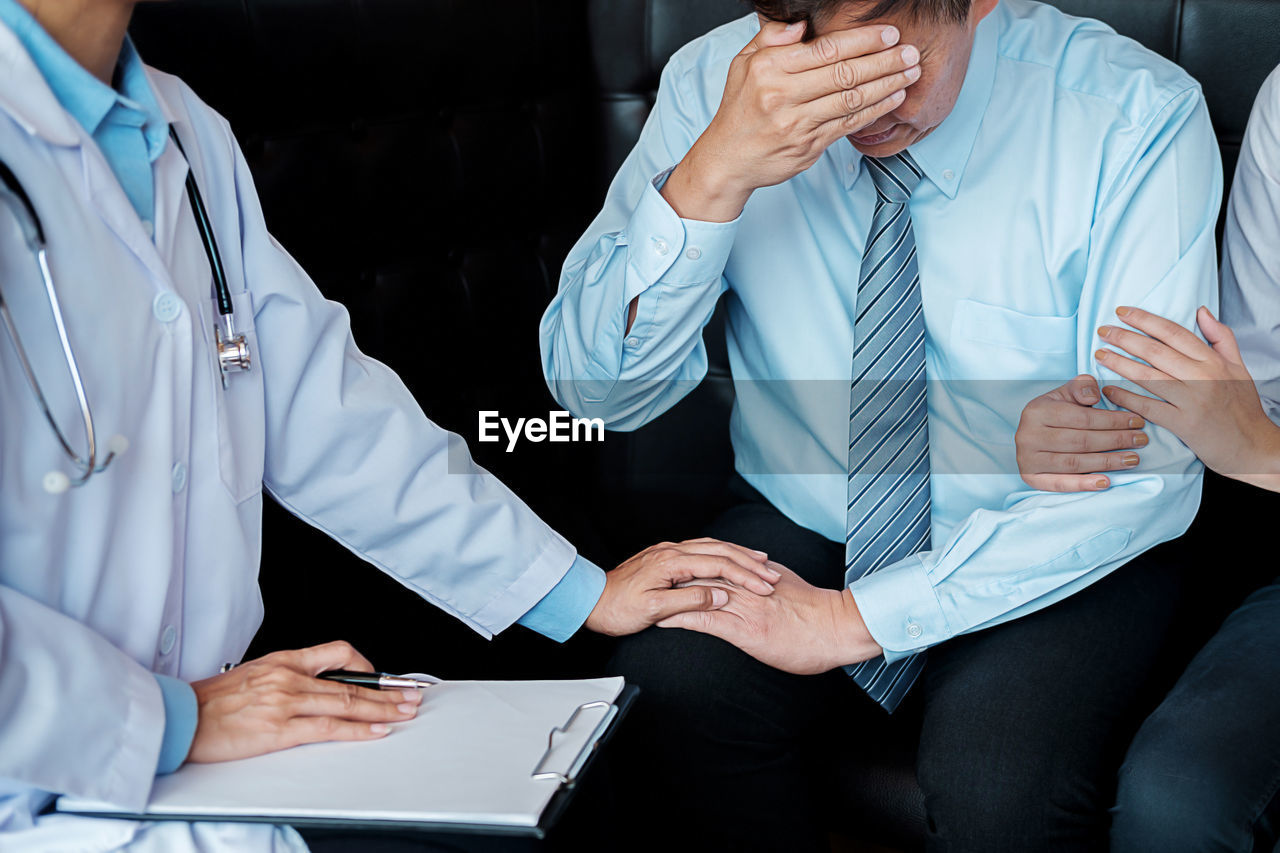 Midsection of doctor consoling patient while sitting on sofa in hospital