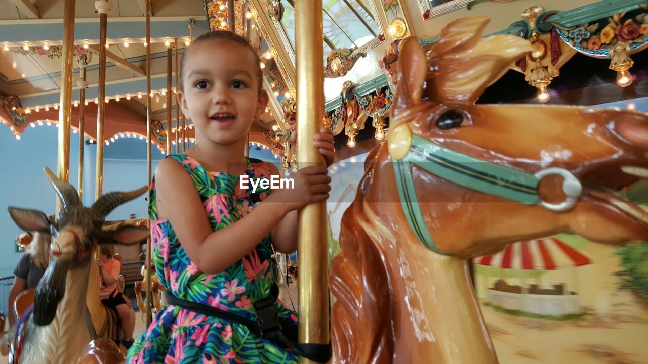 Low angle view of girl sitting in carousel at amusement park