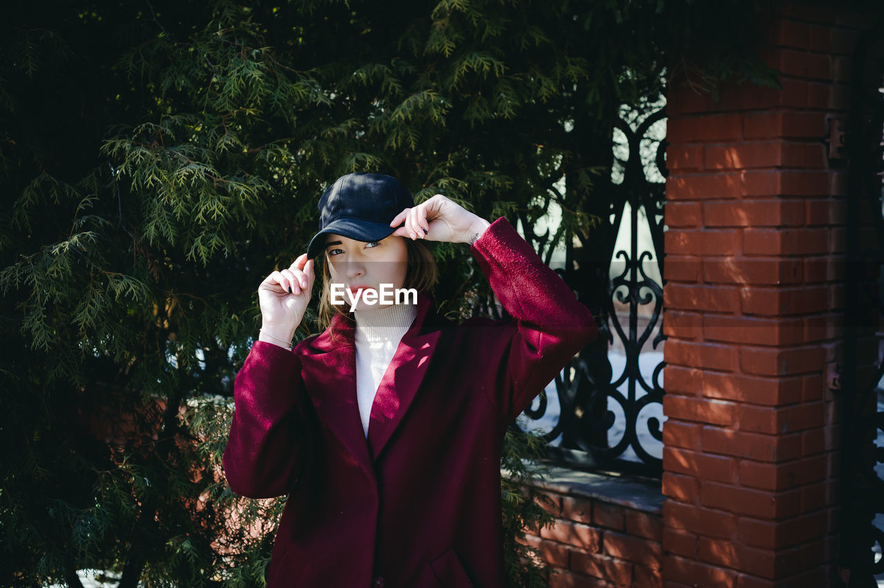 YOUNG WOMAN LOOKING AWAY WHILE STANDING AGAINST WALL