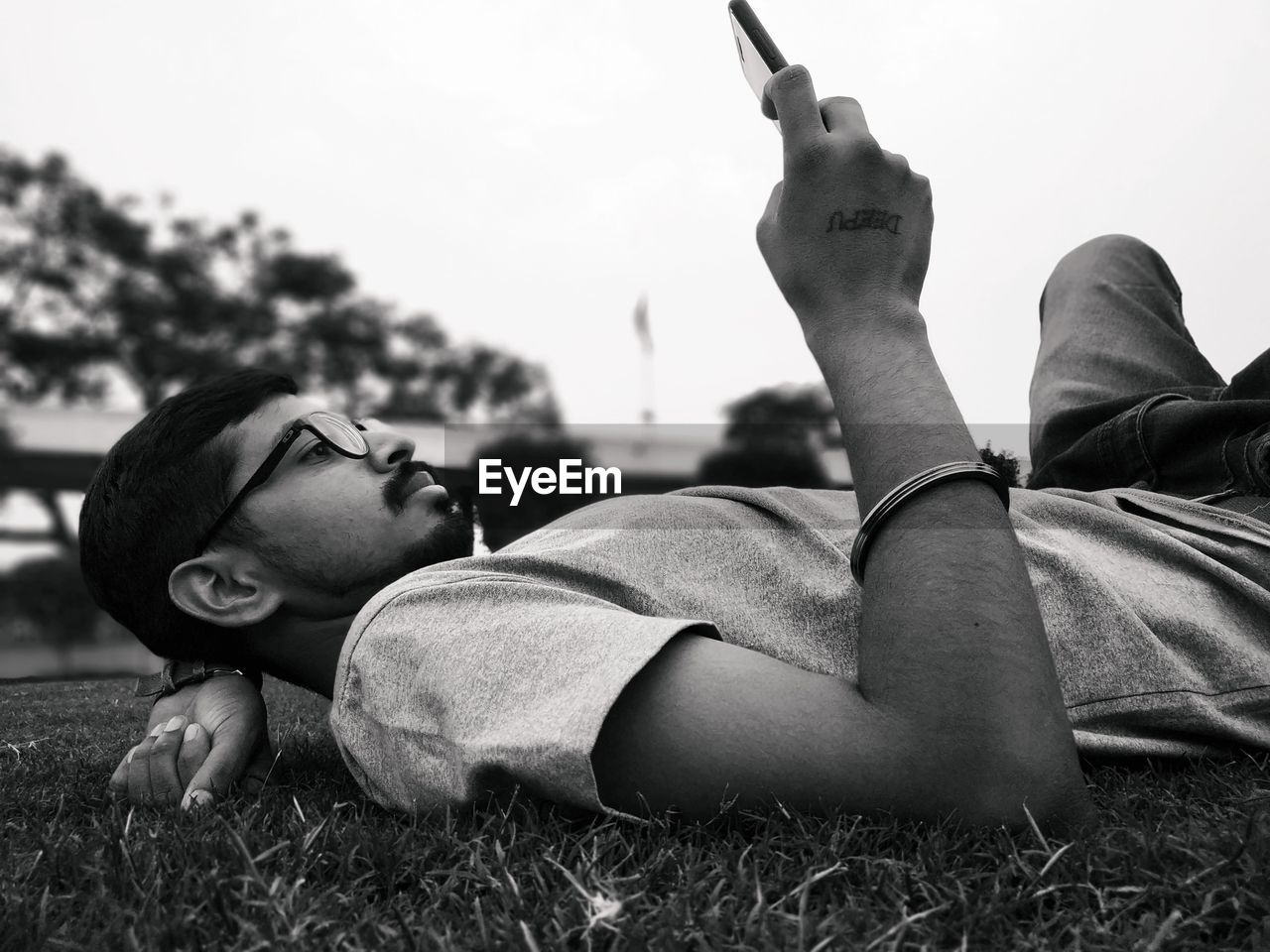 Man using mobile phone while lying on grass against sky
