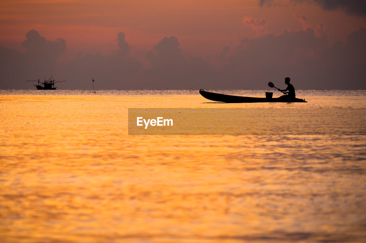 SILHOUETTE MAN ON BOAT IN SEA AGAINST ORANGE SKY