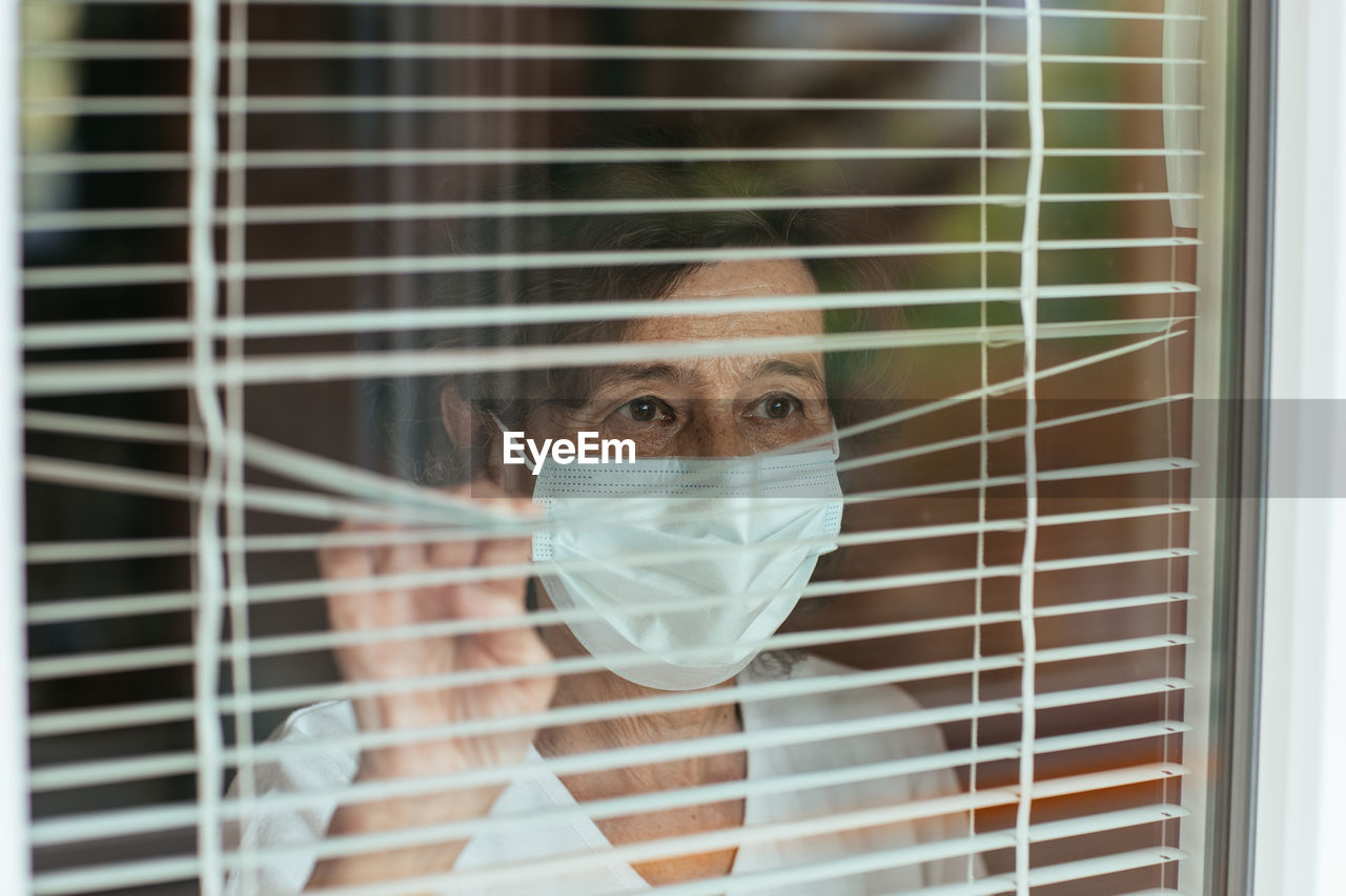 Woman wearing mask looking through window