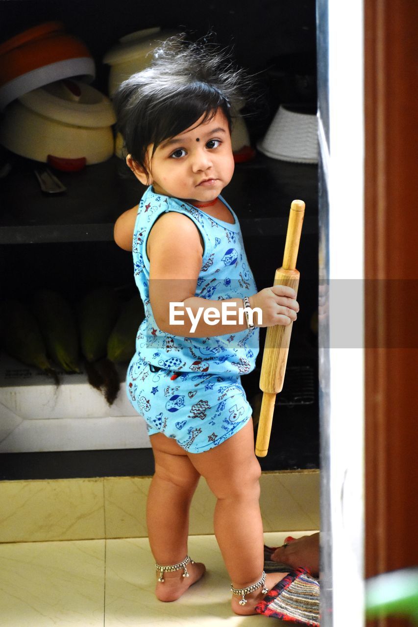 Full length portrait of cute baby girl holding rolling pin at home