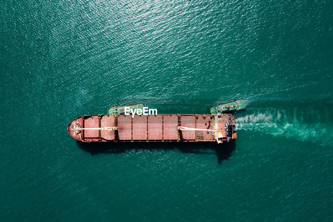 Red oil ship tank and tugboat sailing on green sea photograph aerial from drone point of view