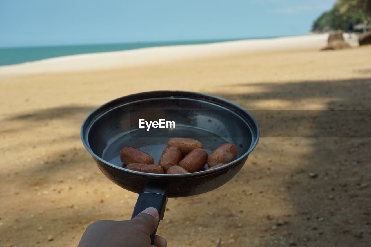 Cropped hand of person holding cooking pan with food at beach