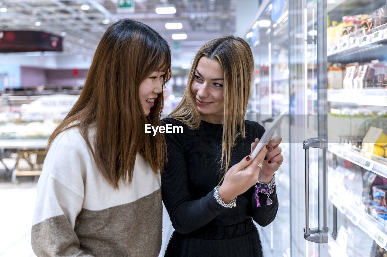 Multi-ethnic couple of young women looking at the shopping list on the tablet at the mall