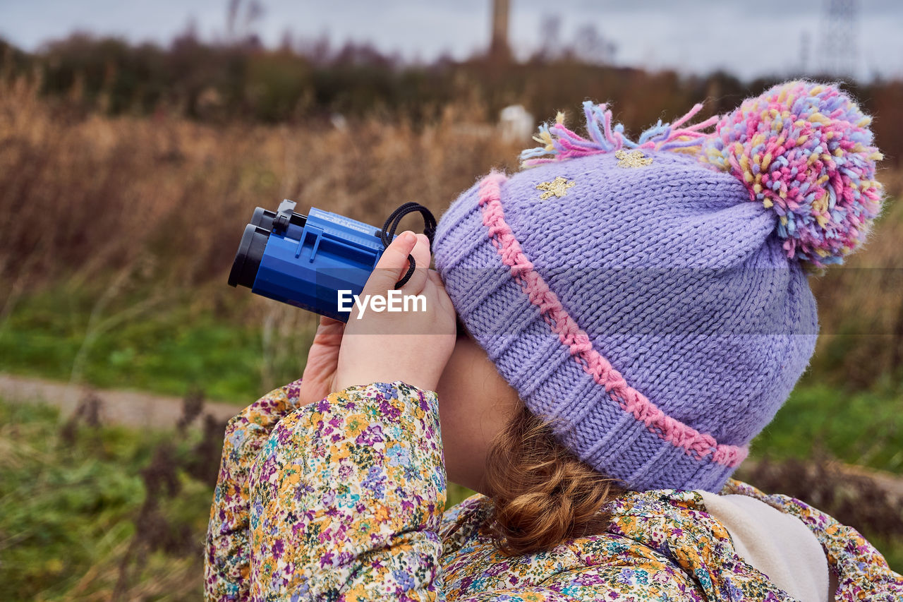 Girl looking through binoculars by plants