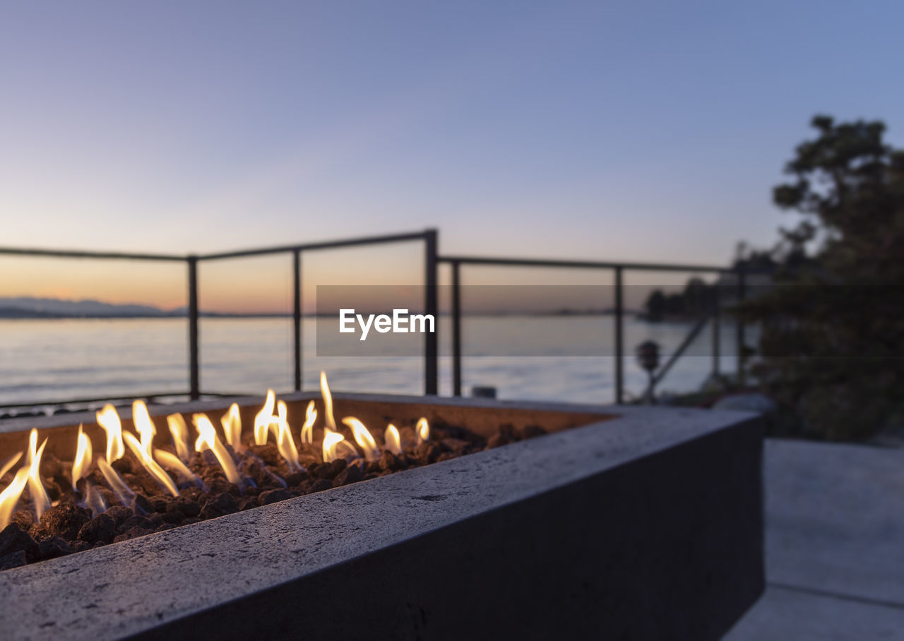 Backyard gas lit fire pit at golden hour blue hour sunset by the waters edge. copy space, no people.