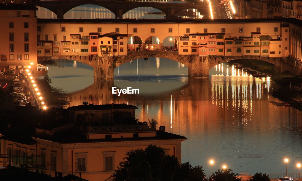 Illuminated bridge over river in city at sunset