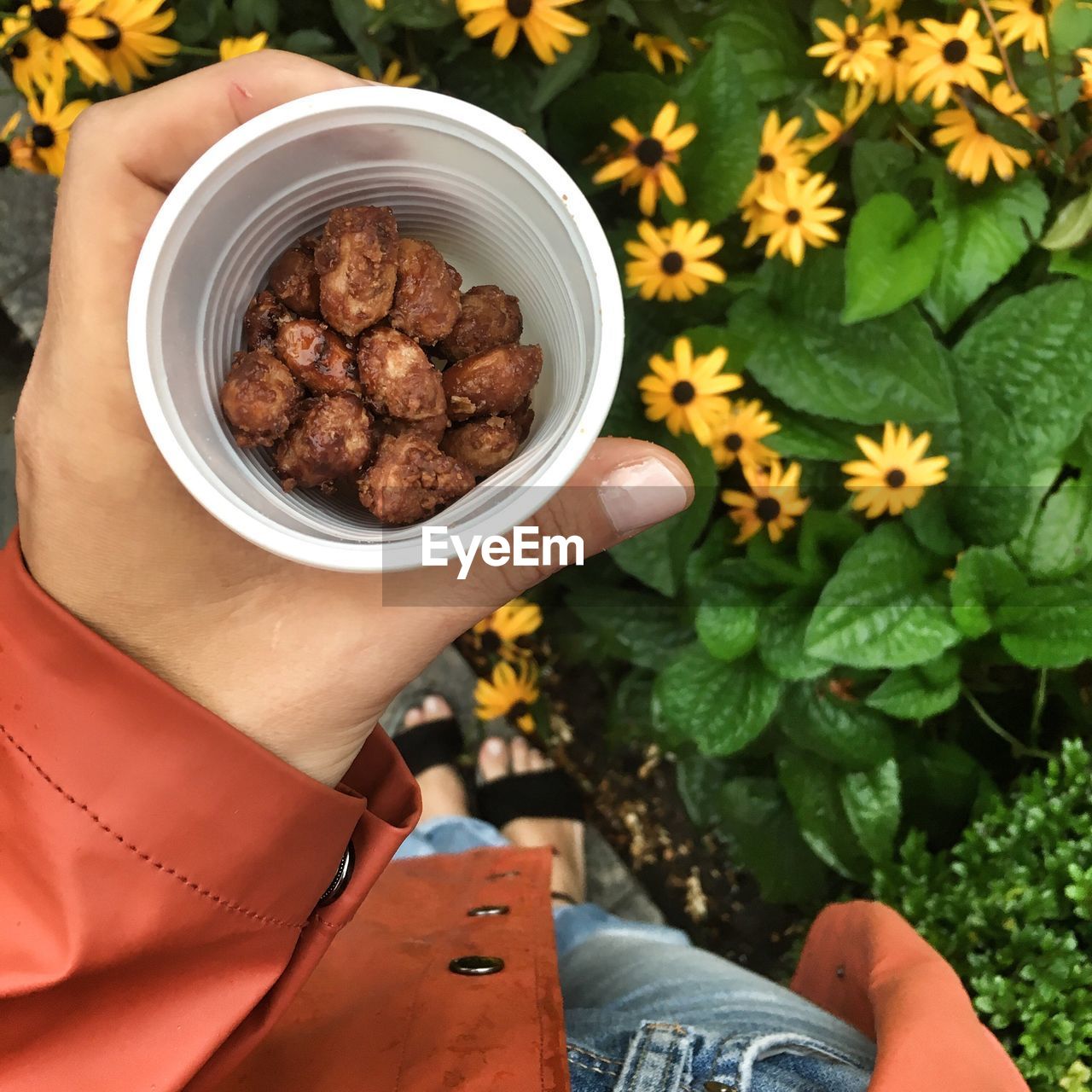 Low section of woman holding caramelized nuts by yellow flowers