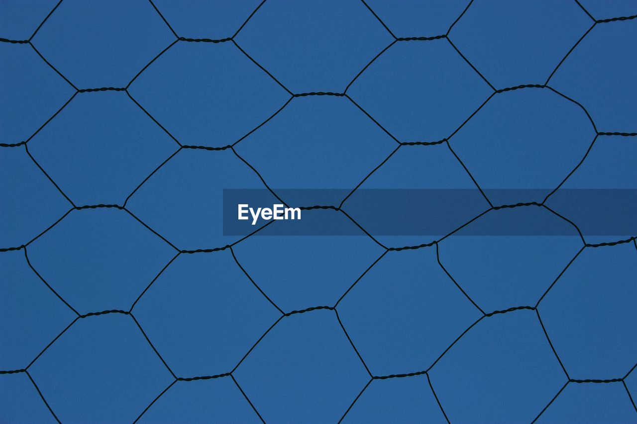 Low angle view of blue sky seen through chainlink fence