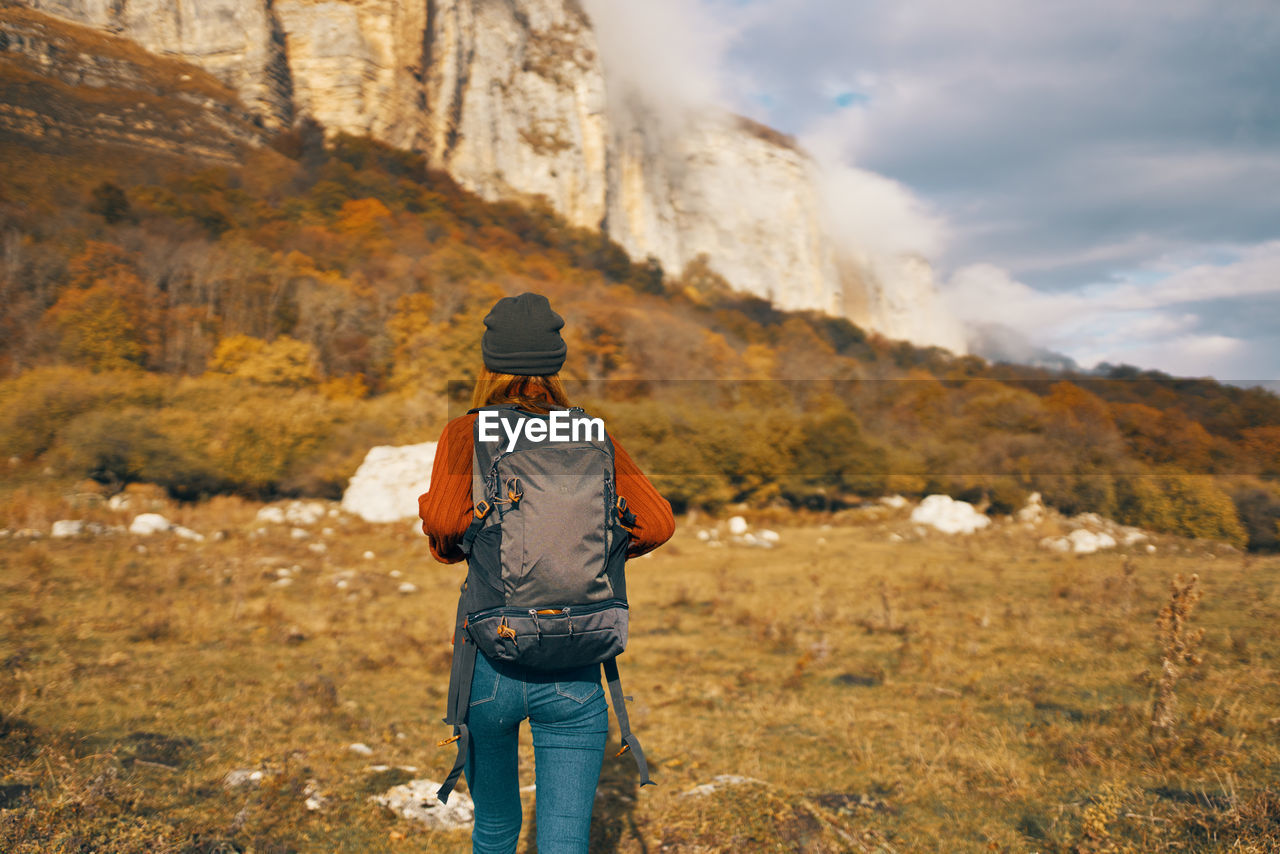 REAR VIEW OF MAN STANDING AGAINST MOUNTAIN