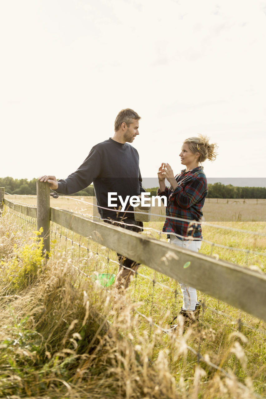 Couple communicating while standing on grassy landscape at farm