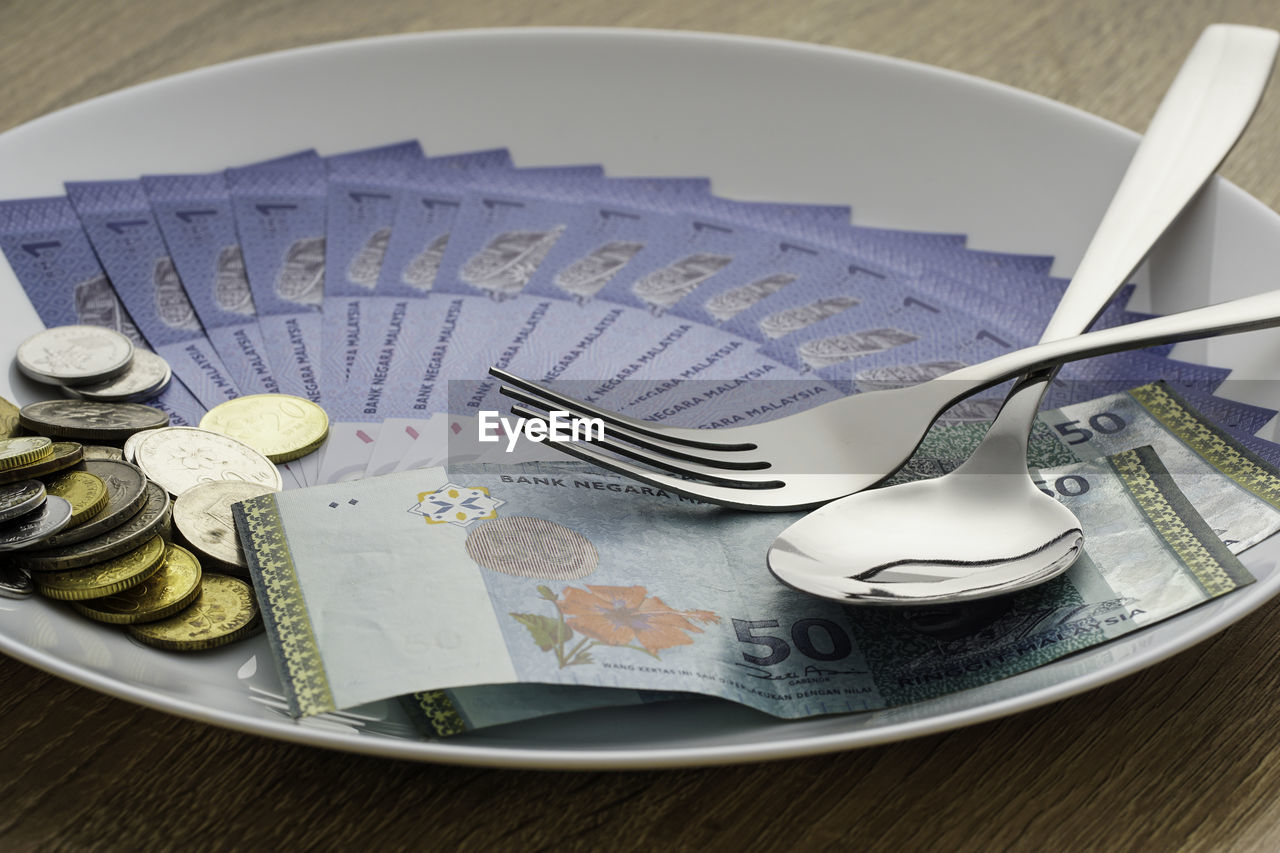 Image of fork, spoon, banknote and coins in a white plate. bribery concept