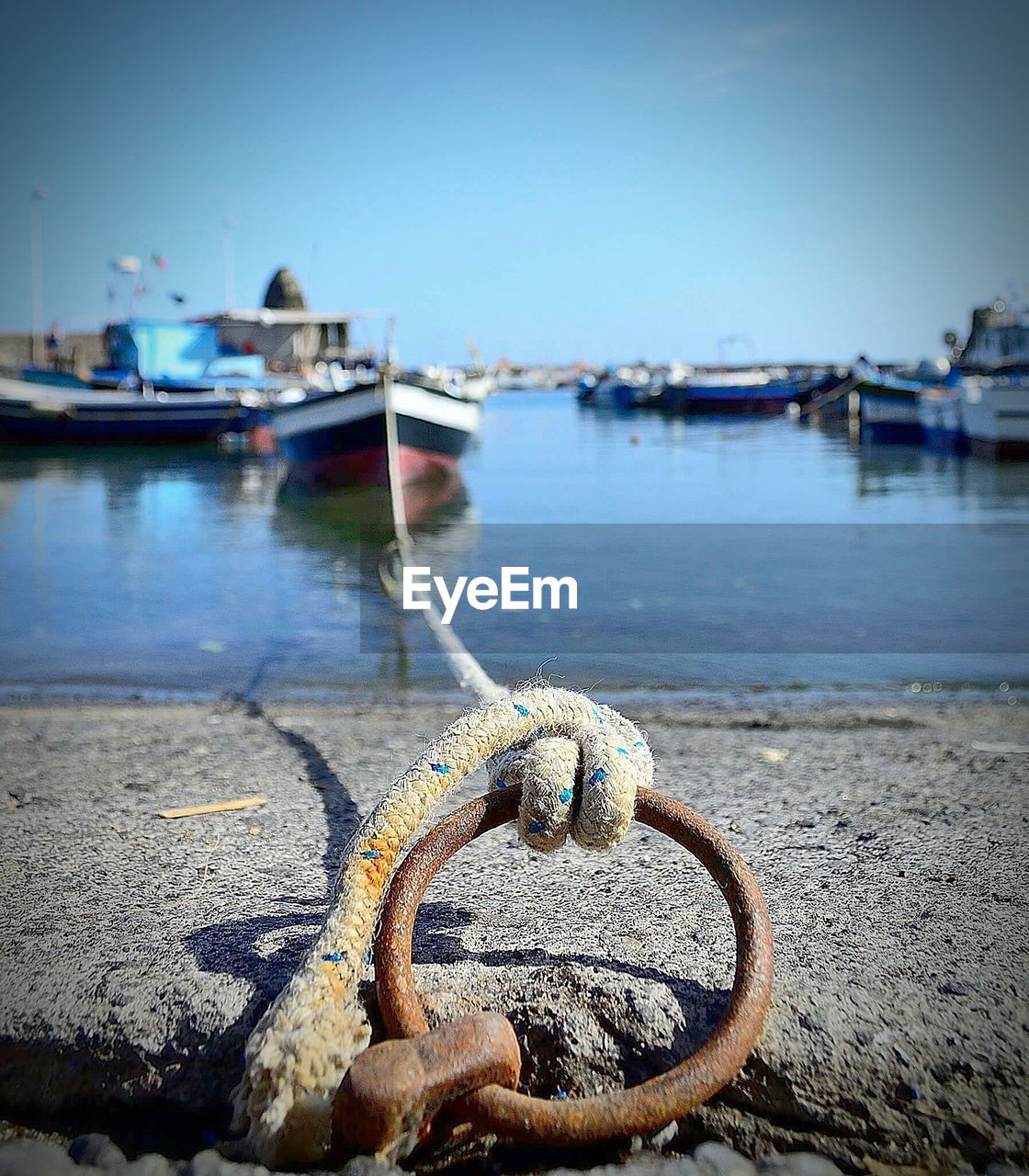 Boat tied up from rope on mooring ring at harbor against clear blue sky