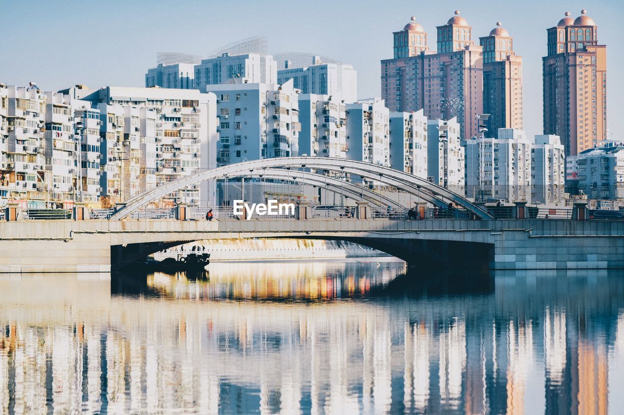 Bridge over river by buildings against sky in city