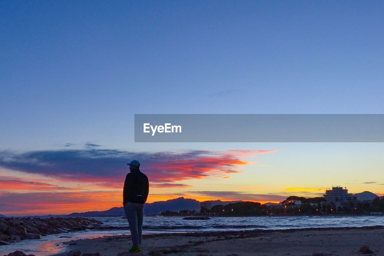 Silhouette man standing on beach during sunset