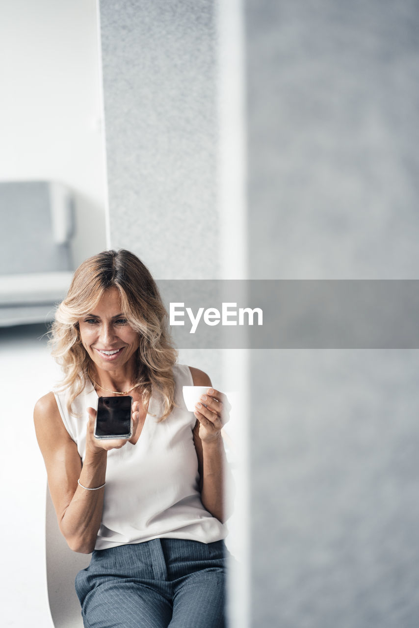 Businesswoman with coffee cup talking on speaker phone sitting at office