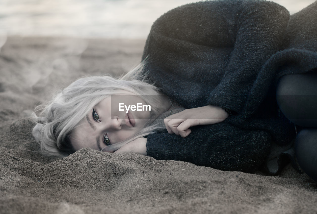 High angle view of thoughtful woman lying on sand at beach