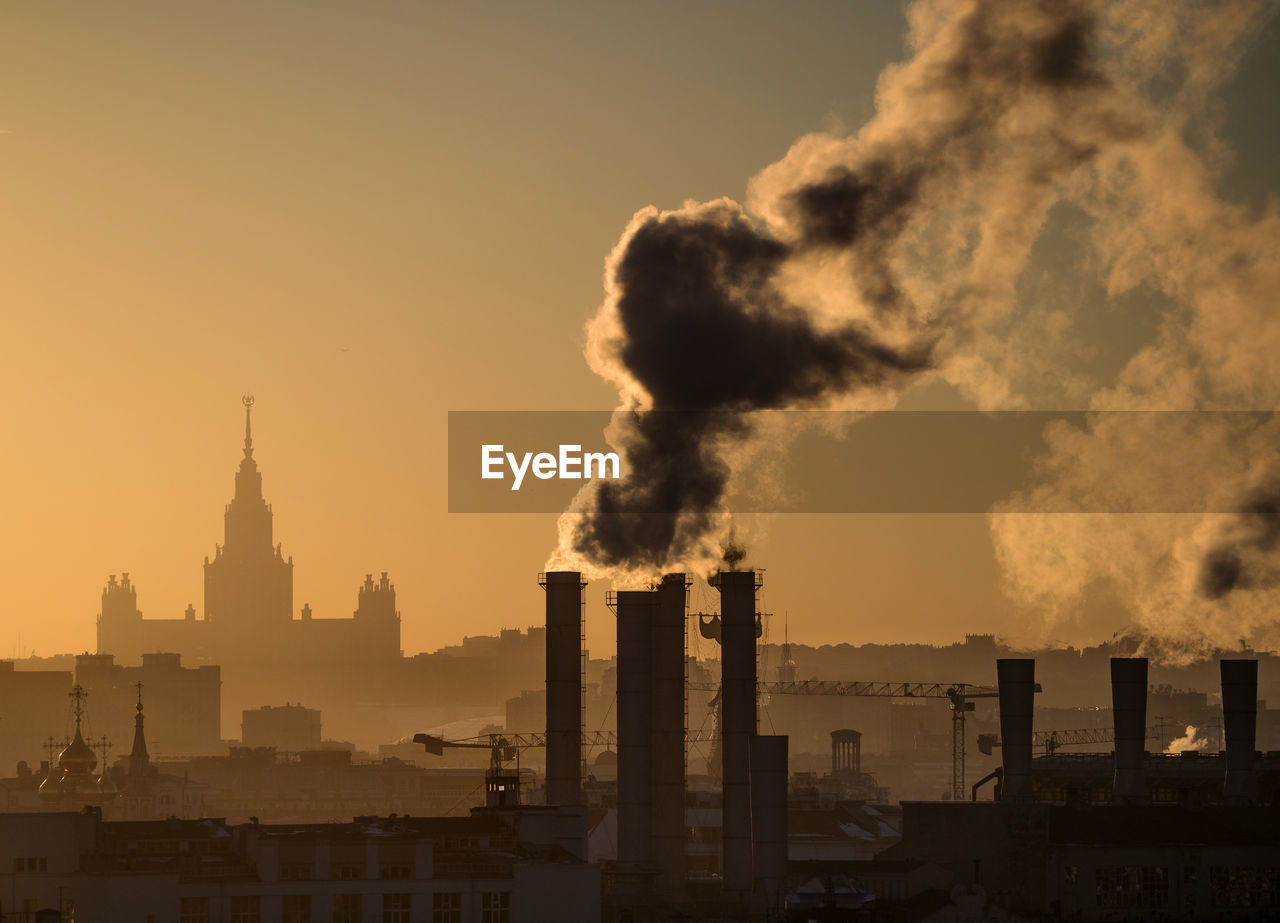 Smoke emitting from chimney at factory against sky during sunset