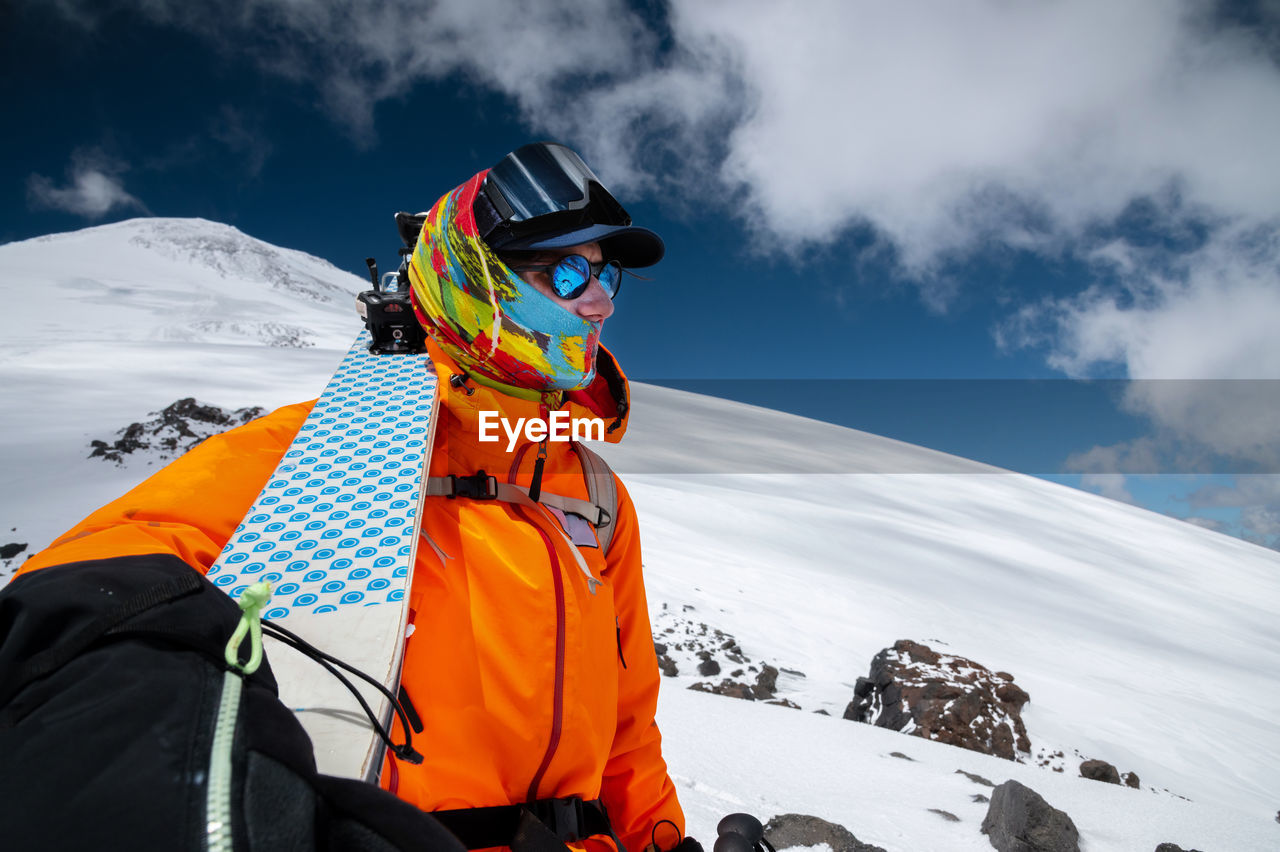 Wide angle shot young tall professional skier holds his skis while standing high in the mountains 