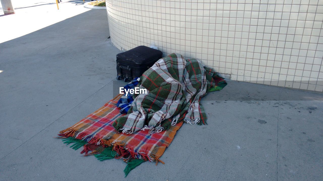 Person sleeping on street in blanket by luggage