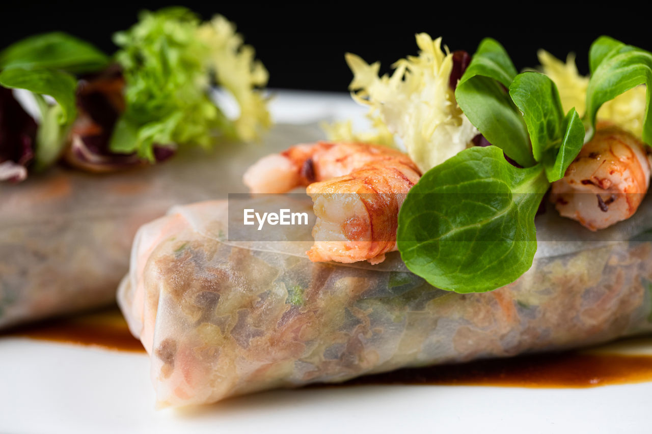 Closeup of delicious duck cannelloni garnished with shrimps and greenery and served on plate in asian restaurant