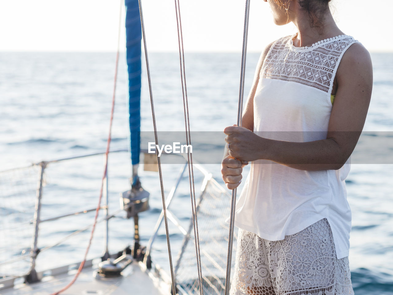 Midsection of mid adult woman holding rope while standing in sailboat on sea