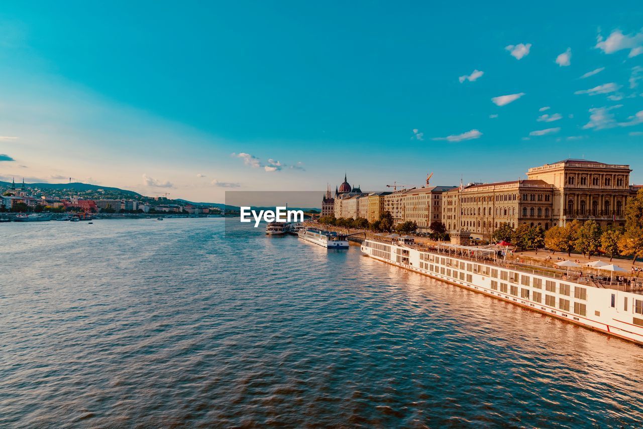 Buildings by river against blue sky