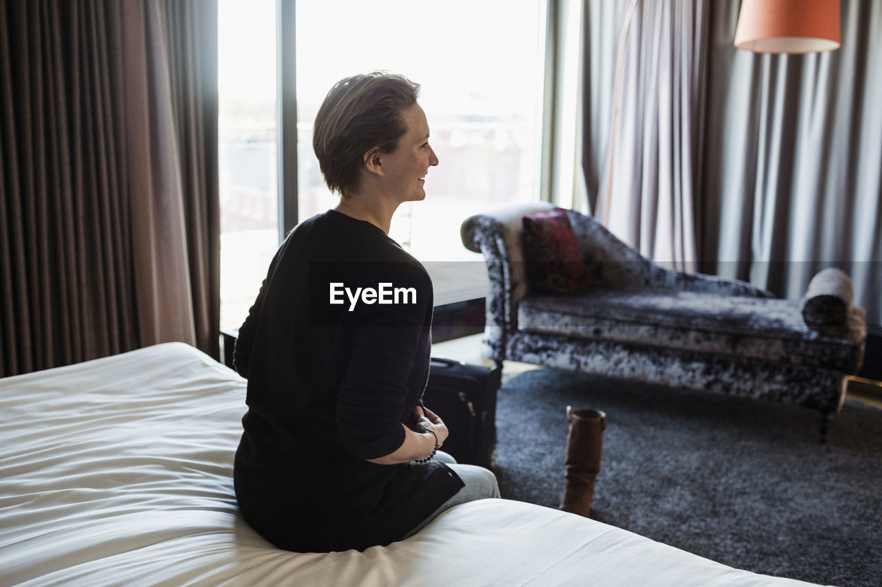 Rear view of smiling businesswoman sitting on bed in hotel room