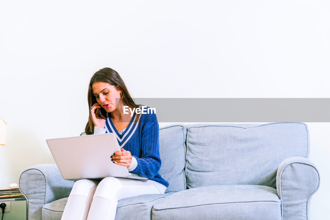YOUNG WOMAN USING PHONE SITTING ON SOFA