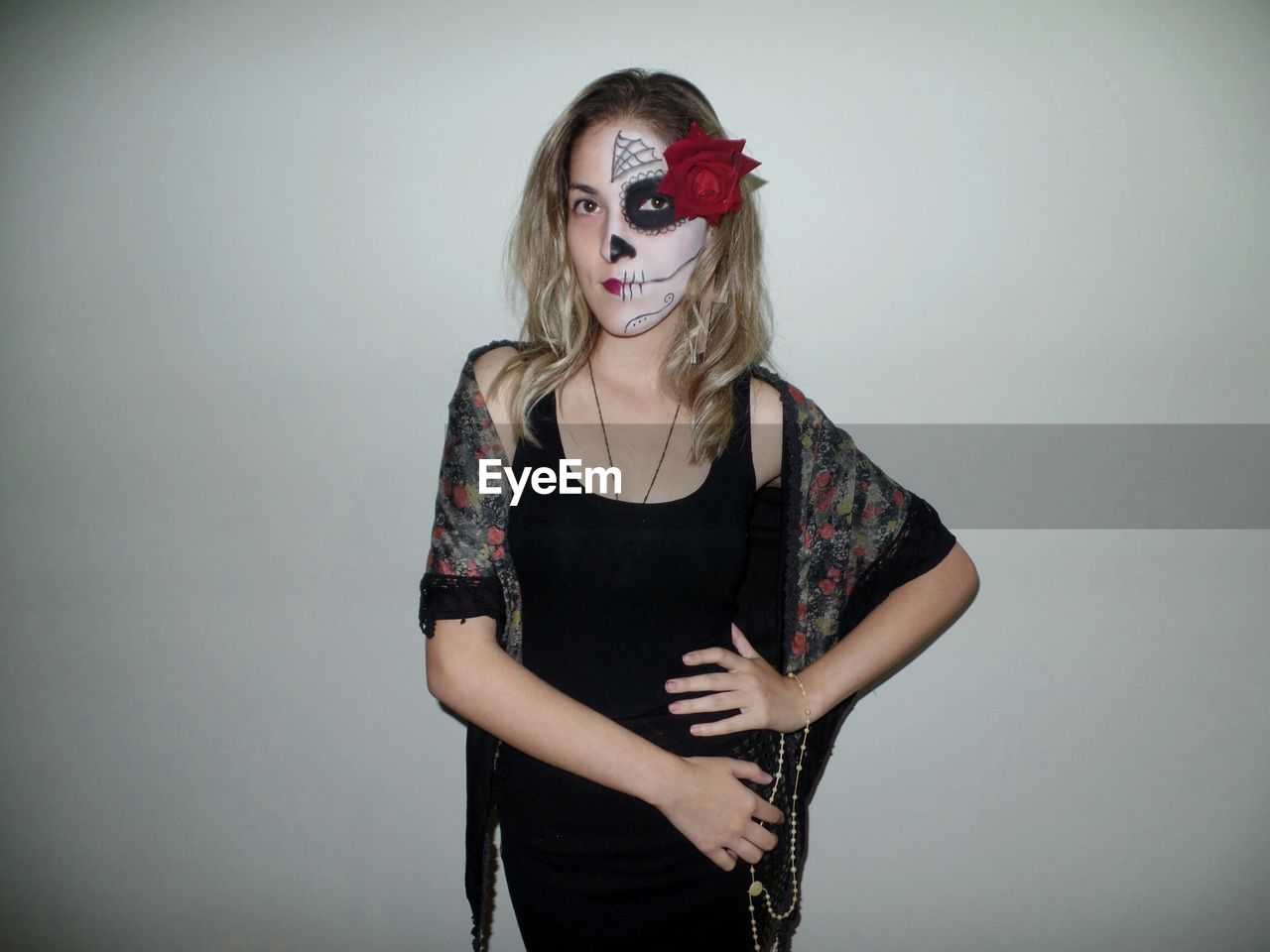 Portrait of young woman with painted face standing against wall