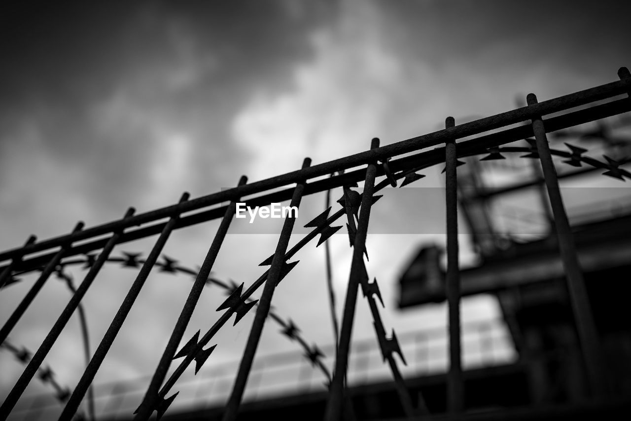 sky, monochrome, black and white, fence, metal, darkness, cloud, black, protection, light, monochrome photography, security, no people, line, architecture, low angle view, nature, wire fencing, wire, outdoors, warning sign, barbed wire, built structure, silhouette, sign