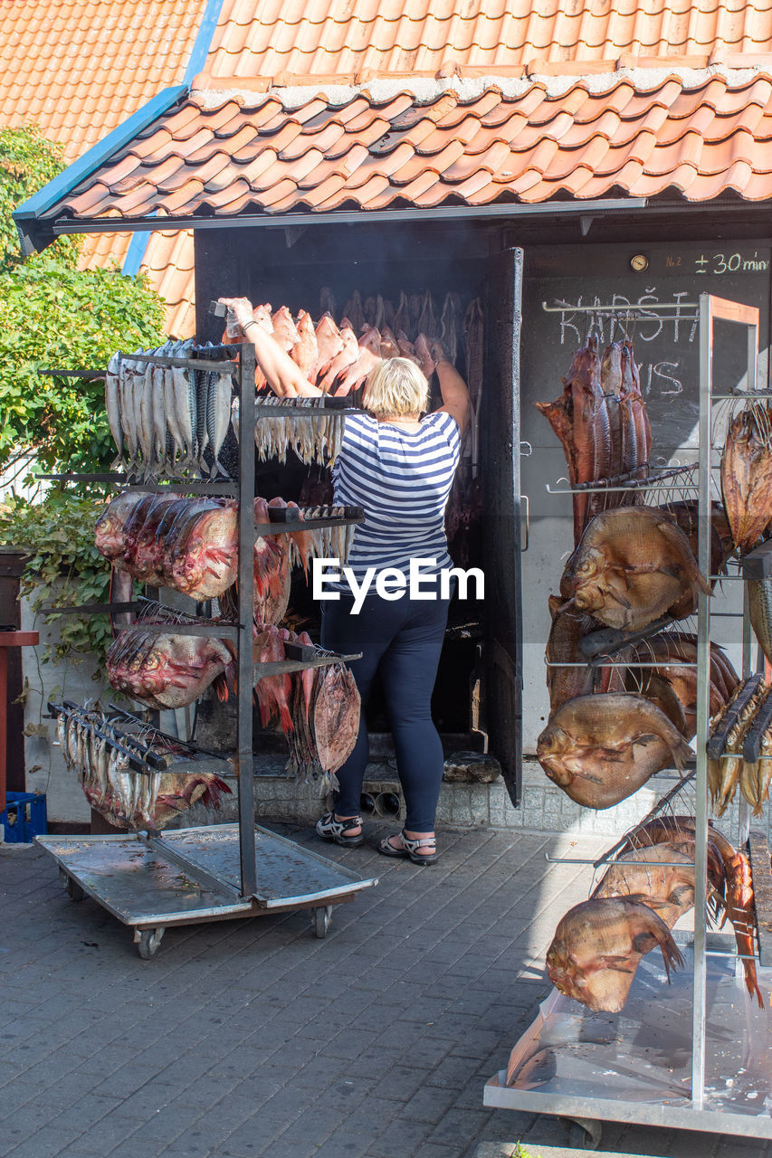 REAR VIEW OF WOMAN STANDING BY MARKET STALL FOR SALE