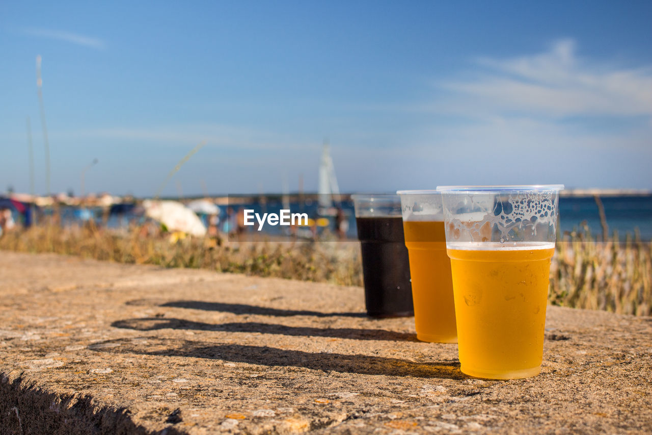 Close-up of three beers on table at beach against sky
