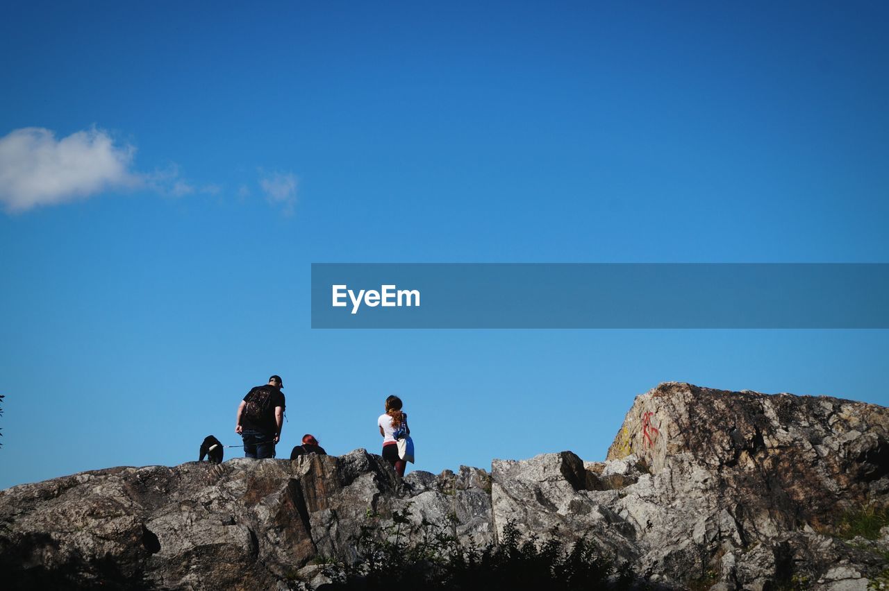 Low angle view of people on cliff against blue sky