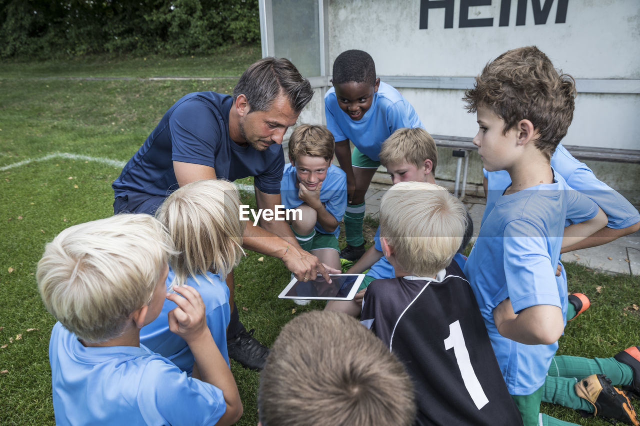 Coach with tablet and young football players on football ground