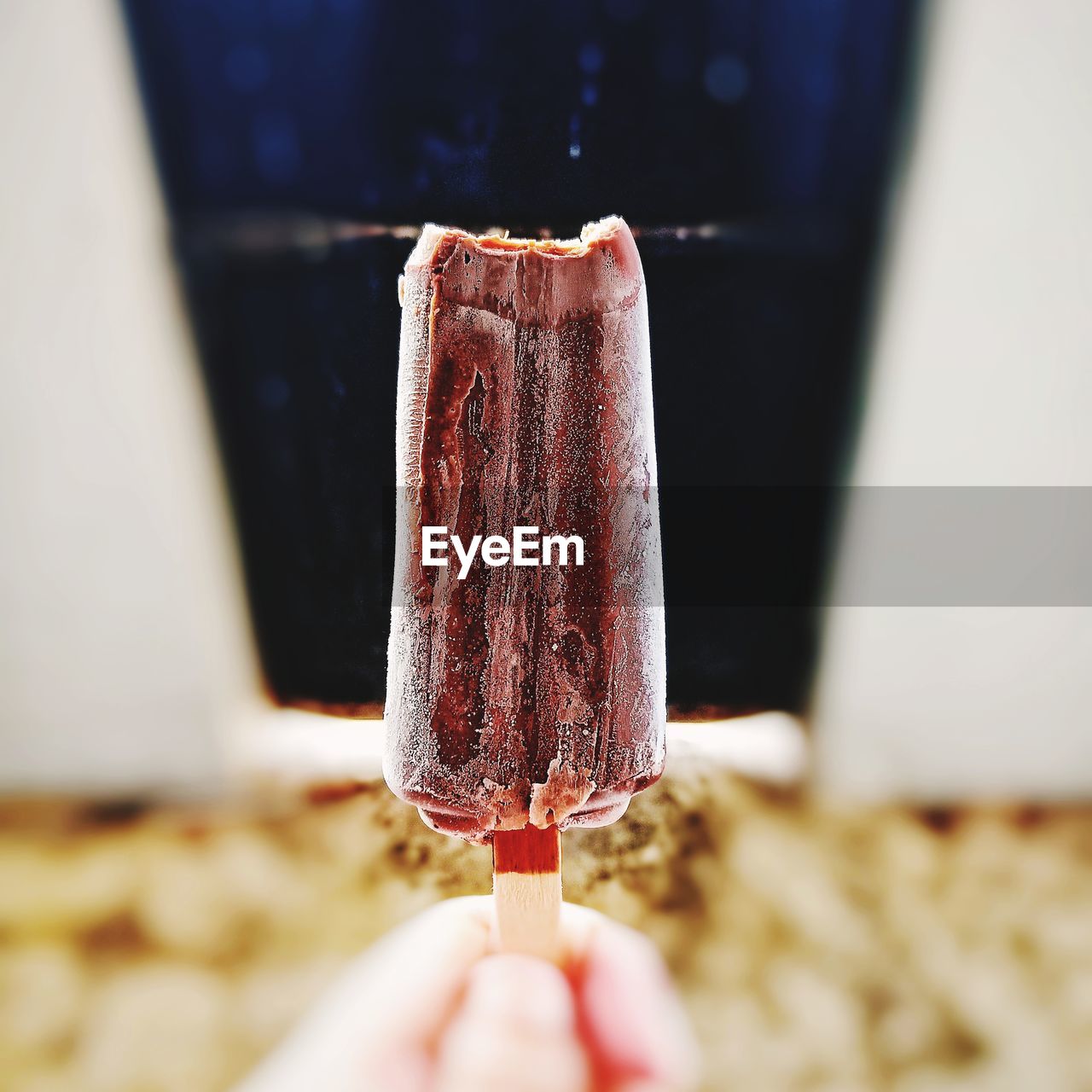 CROPPED HAND HOLDING ICE CREAM CONE AGAINST BLURRED BACKGROUND