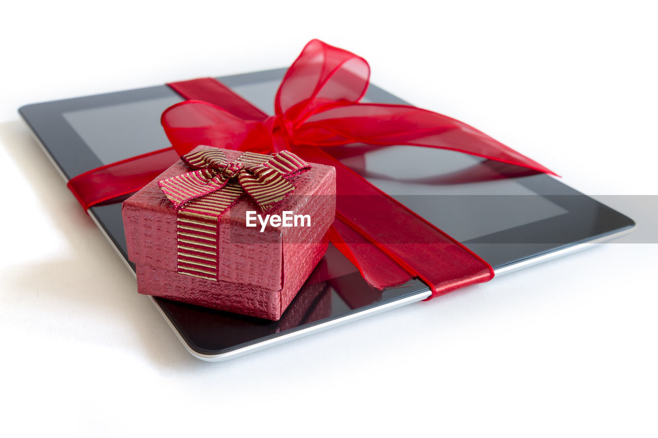 Close-up of digital tablet covered with ribbon and gifts on white background