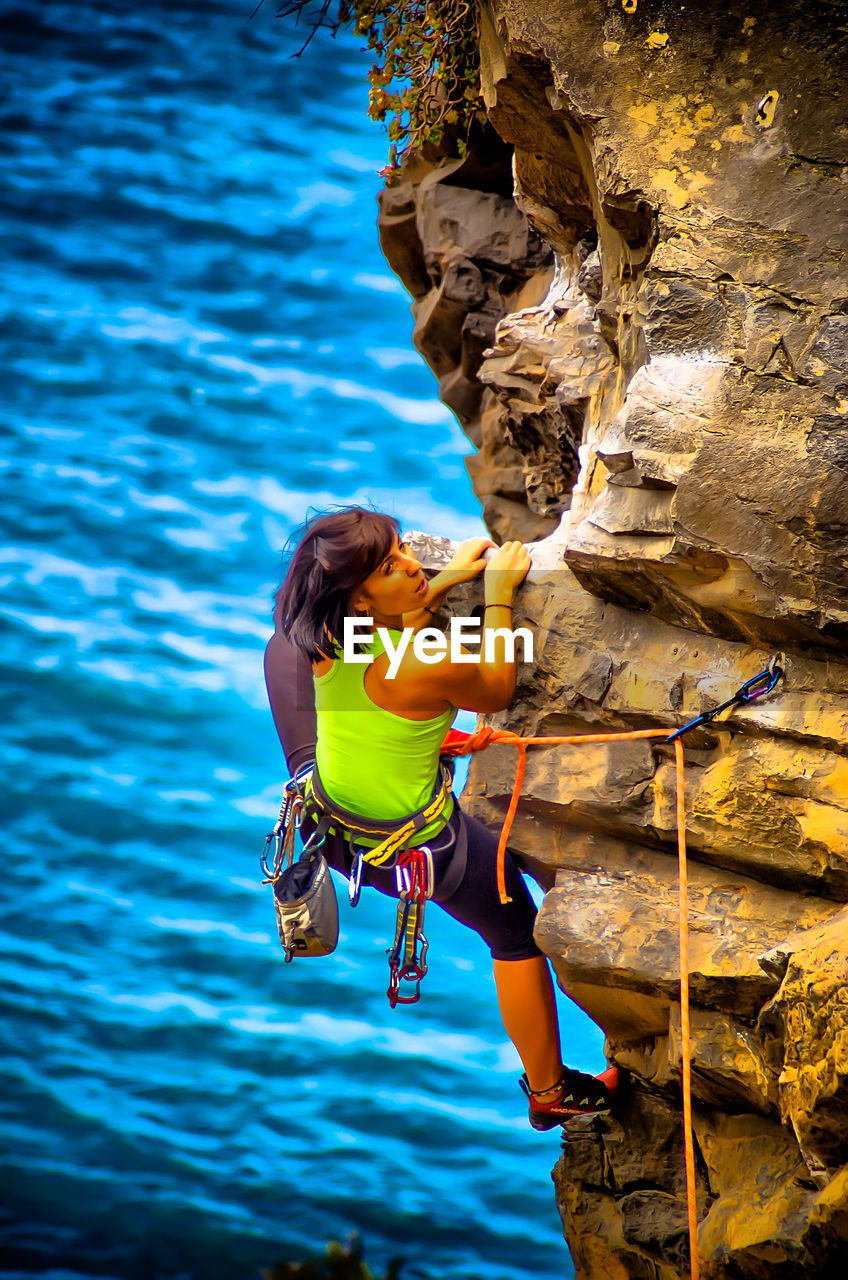 High angle view of hiker climbing cliff against sea
