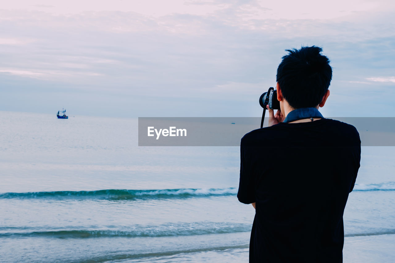 Rear view of man photographing against sea and sky