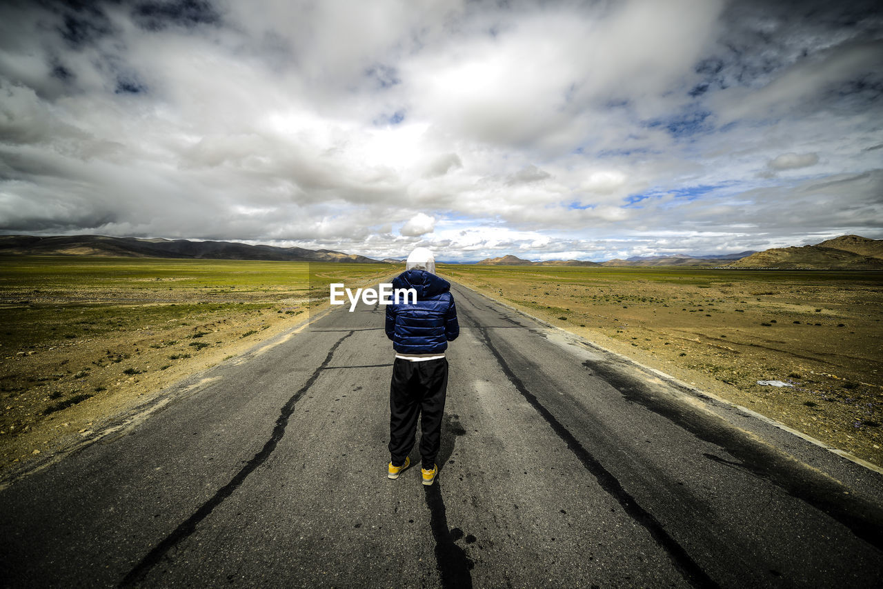 Rear view of woman on road amidst landscape against storm clouds