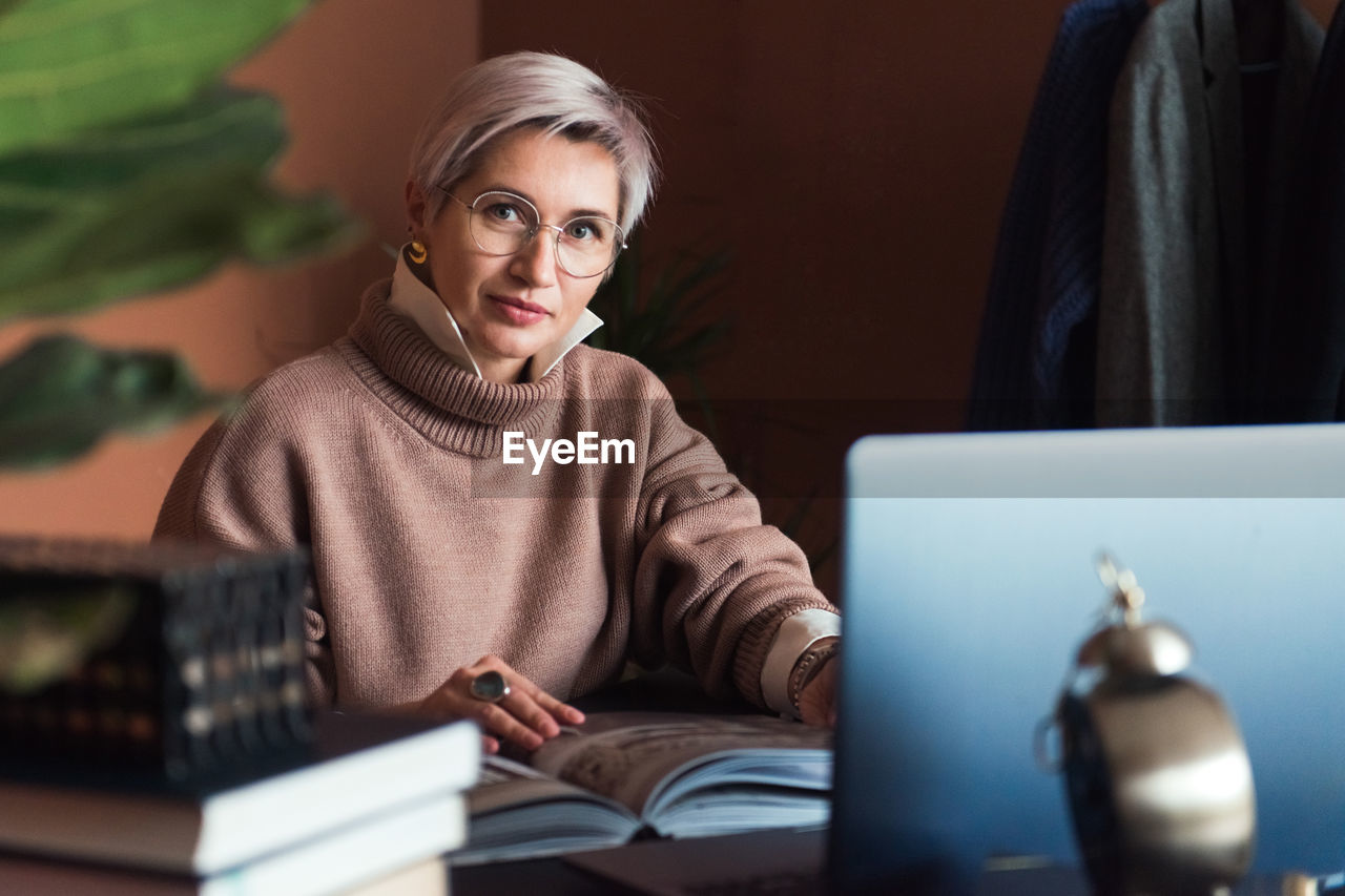 Fashion woman in brown oversize sweater working in modern work place or office with laptop