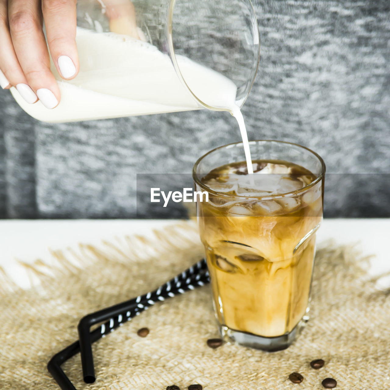 Close-up of hand holding pouring milk in cold coffee on table