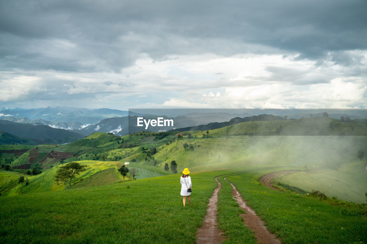 REAR VIEW OF MAN ON DIRT ROAD AMIDST LANDSCAPE