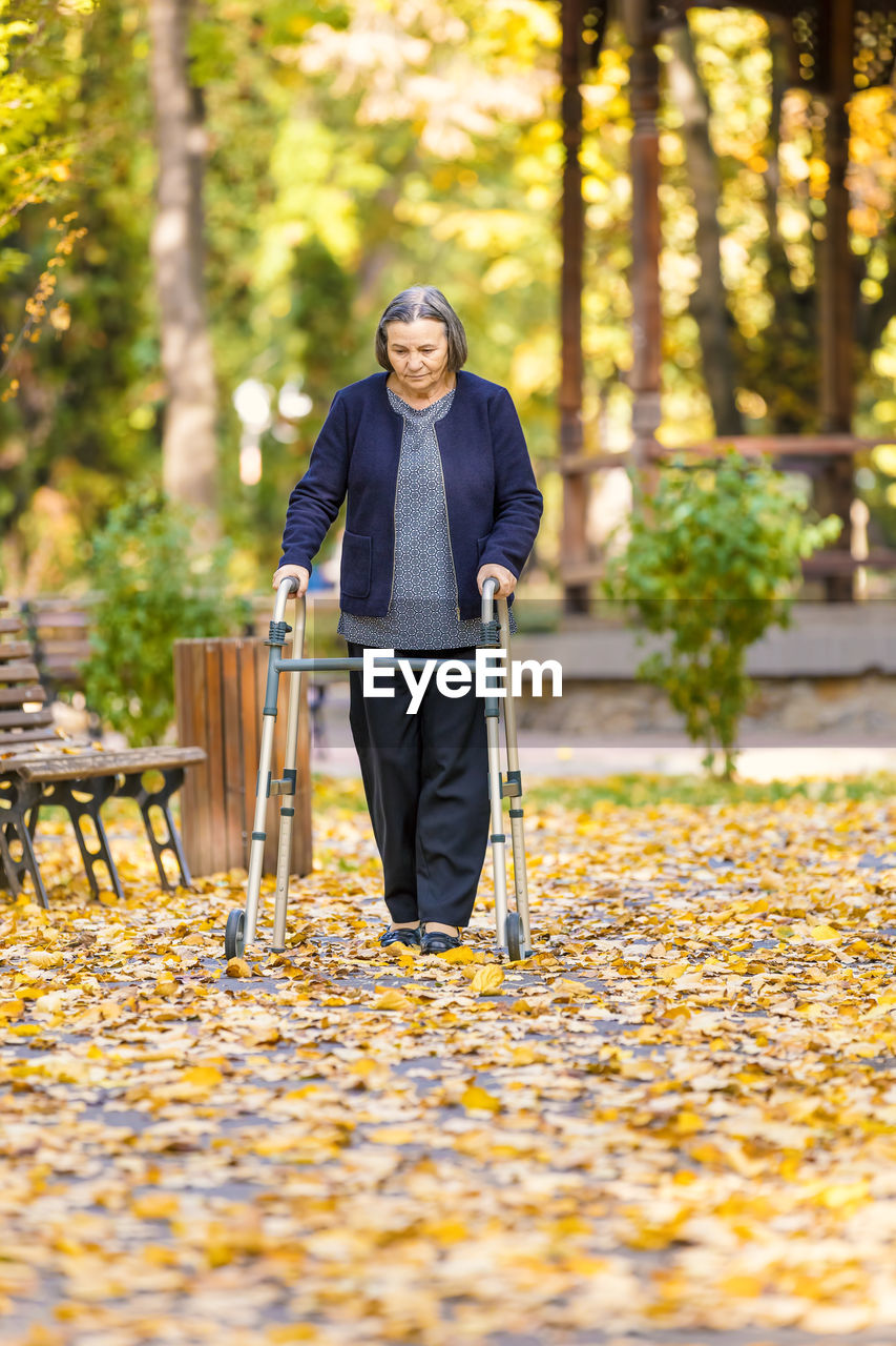 Senior woman with mobility walker walking at park during autumn