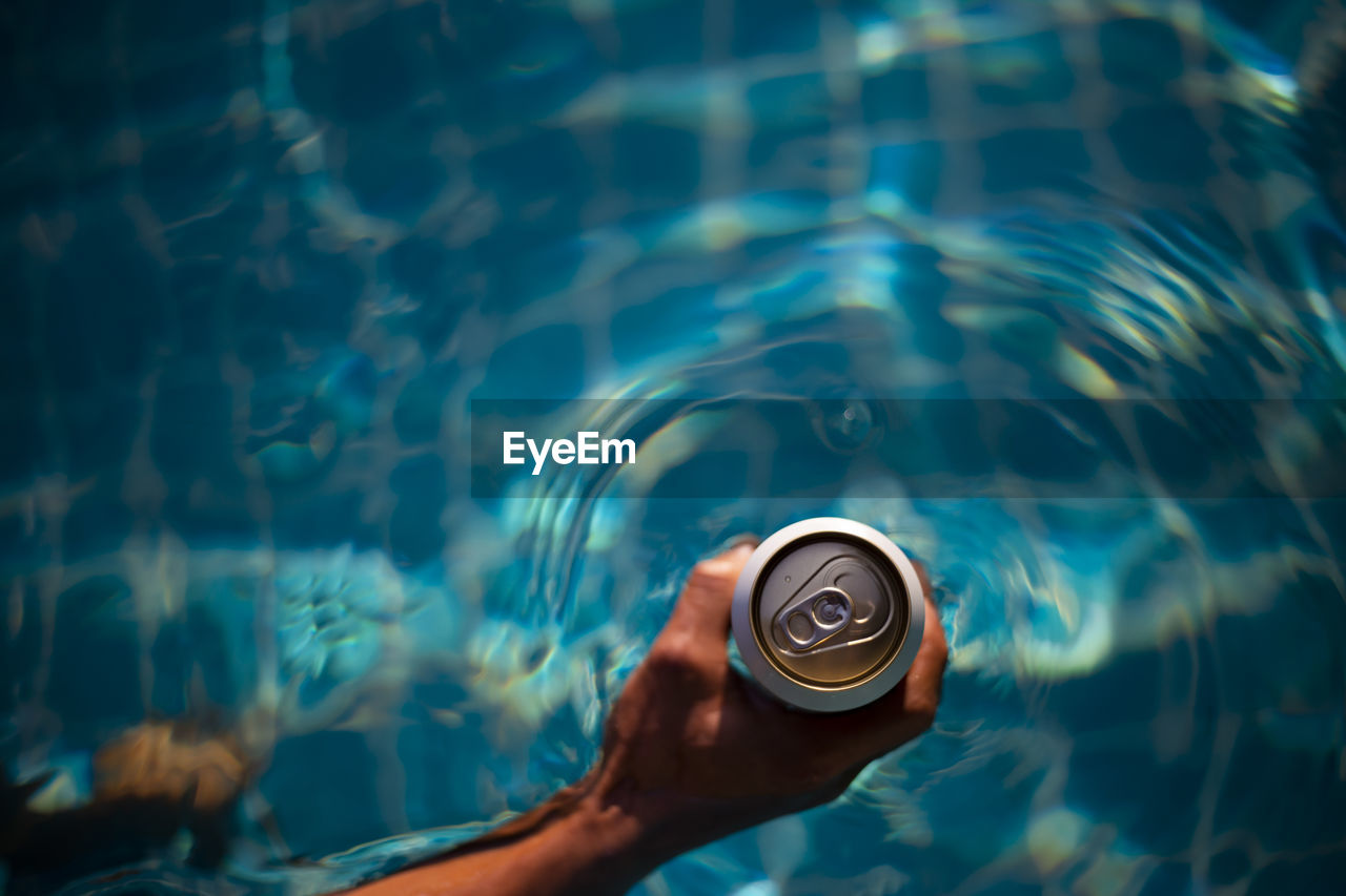 Selective focus white beer can in hand. man is soaking in the pool with an open 