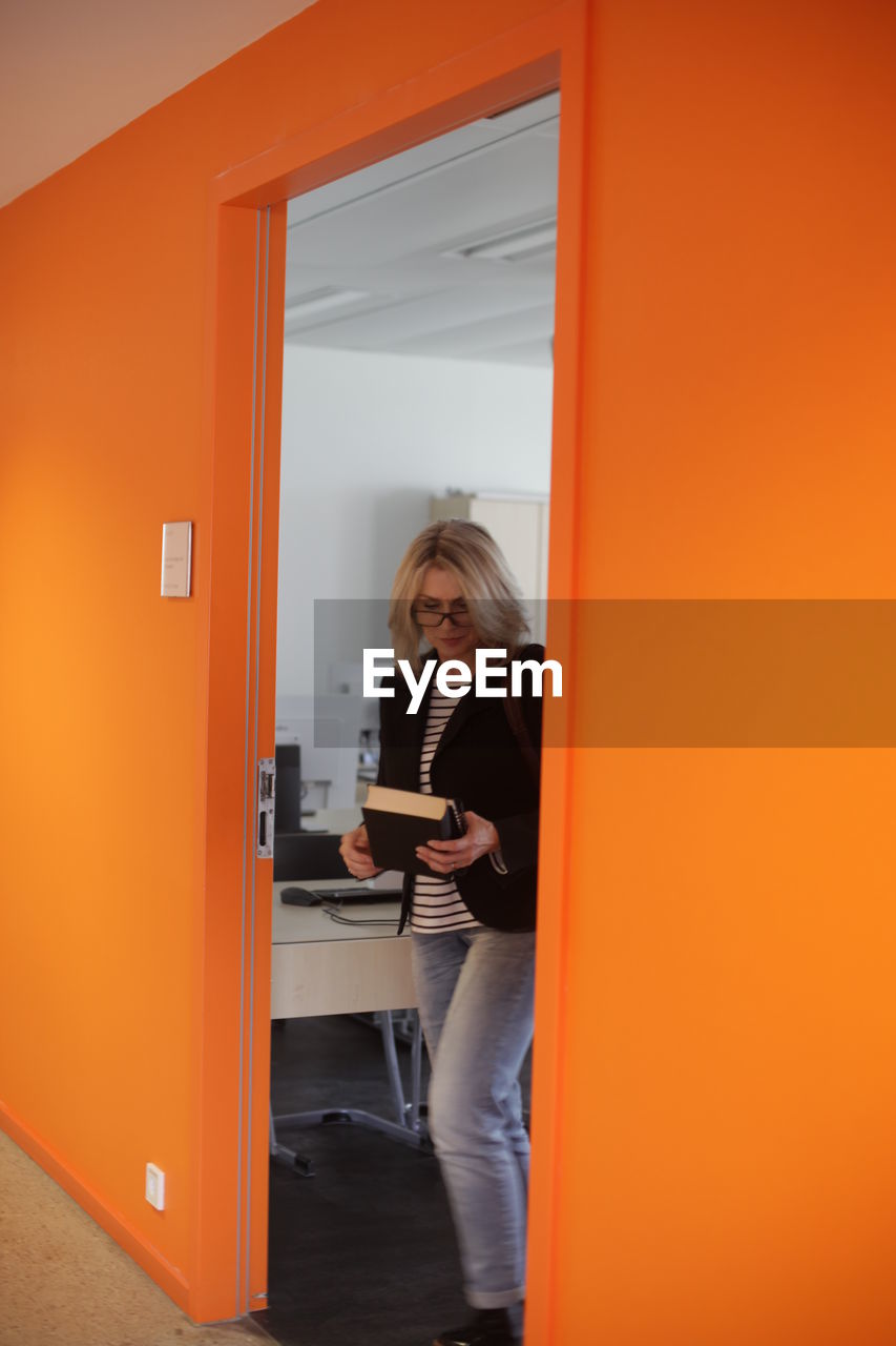 WOMAN STANDING BY DOOR OF ORANGE