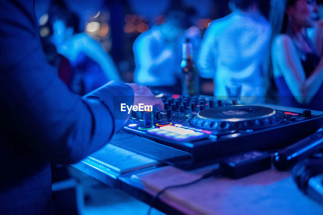 Midsection of man operating sound mixer with people in background in music concert at night