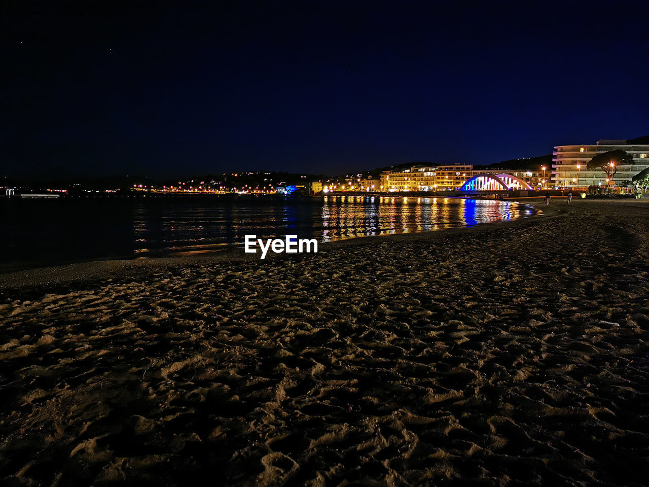 ILLUMINATED CITY BY SEA AGAINST SKY AT NIGHT